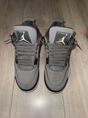 Gråa Air Jordan 4  - Snygga Air Jordan 4 Retro sneakers i olika grå nyanser med svarta och vita detaljer. Skorna har den klassiska Jumpman-loggan på plösen och tjocka grå skosnören. Ovandelen är i mocka och mesh för en sportig look. - använda ett fåtal gånger men har små scratches( bild 5 ) syns knappast