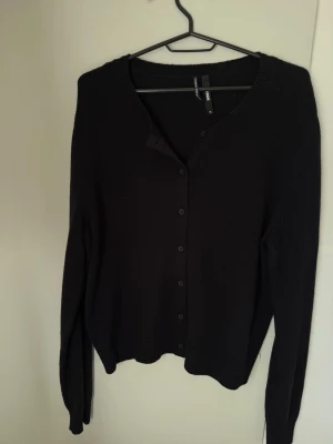Svart kofta från BikBok cashmereull - Snygg svart kofta från BikBok i cashmere- och ullblandning. Klassisk modell med knappar framtill, rund halsringning och långa ärmar. Perfekt att slänga över en t-shirt eller linne för en chill look.
