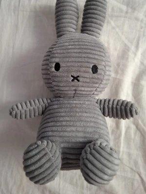 Grå Miffy kanin i manchestertyg - Supergullig grå Miffy-kanin i mjukt manchestertyg med broderade svarta ögon och nos. Klassisk rund form med långa öron och tydliga ränder i tyget. Perfekt som prydnad eller gosedjur. Märkt med etikett på baksidan.