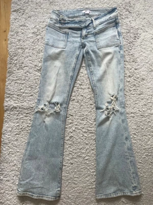 Ljusblå bootcut jeans från Gina  - Säljer ett par ljusblå bootcut jeans från Gina  med slitna detaljer och hål på båda knäna. Jeansen har stora framfickor och en cool tvättad look. 