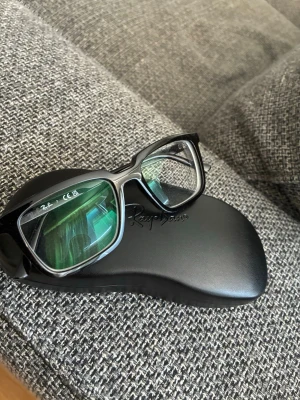 Ray-Ban RB7239 ALAIN - Säljer ett par Ray-Ban RB7239 ALAIN glasögonbågar i svart färg. Glasögonen är helt oanvända och kommer med allt originaltillbehör. Modell: Ray-Ban RB7239 ALAIN Storlek: 52-18 Skalmlängd: 145 mm Färg: Svart Viktigt att veta: Glasen som sitter i bågarna har synstyrka och behöver därför bytas ut av köparen. Du får själv besöka en optiker för att sätta in glas med den styrka som passar dig. Perfekt för dig som söker ett par stilrena och högkvalitativa Ray-Ban-bågar