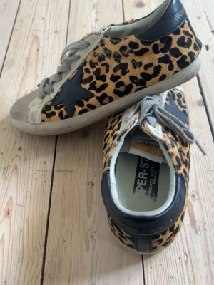 Leopardmönstrade sneakers Golden Goose - Säljer ett par unika sneakers från Golden Goose med leopardmönstrad ovandel i pälsimitation, grå mockadetaljer på tån och snörning samt svart stjärna på sidan. Skorna har vit sula och svart hälparti med logga. Perfekta för dig som vill sticka ut.