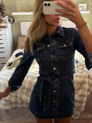 Mörkblå jeansklänning med bälte - Säljer en snygg mörkblå jeansklänning med knappar framtill, bröstfickor och ett matchande knytbälte i midjan💖💖❣️Använd 1 gång!