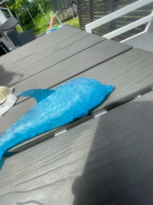 Squshiyyy  - Säljer en blå dekorationsdelfin i plast med glittrig yta. Delfinen har en tydlig fena och svans, och är formad för att likna en riktig delfin. Perfekt som prydnad eller leksak till rummet.