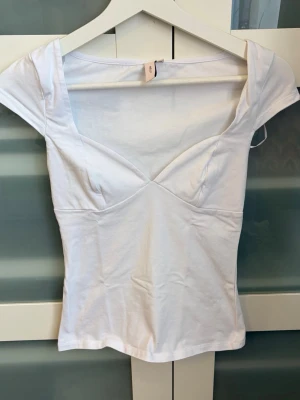 Vit v-ringad topp från Nelly - Snygg vit topp från Nelly med v-ringning och korta ärmar. Figurnära passform och mjukt bomullsmaterial som känns skönt mot huden. Perfekt att styla med jeans eller kjol för en fräsch look.