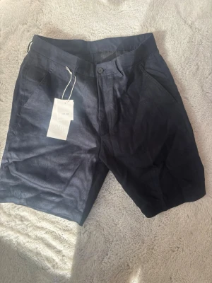 Mörkblåa linneshorts från Zara - Snygga mörkblå shorts i linne med klassisk passform och sidofickor. Shortsen har knapp och gylf framtill samt två bakfickor. Perfekta för varma dagar och ger en clean look. Shortsen är helt nya, bara provade. Säljer för att de var för små. Pris kan diskuteras. Ny pris är 429kr.