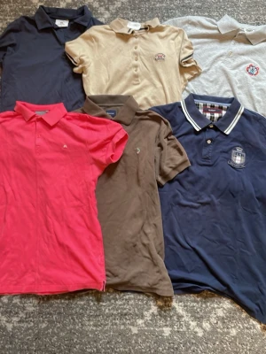 6-pack pikétröjor från GANT & fler - Säljer ett paket med sex pikétröjor i olika färger: marinblå, beige, grå, brun, vinröd/rosa och mörkblå. En av tröjorna är från GANT med broderade loggor och krage med ränder. Alla har klassisk pikékrage och korta ärmar. Perfekt för dig som gillar stilrena och bekväma toppar. Märkerna är Kenzo mindre bra skick som ses på bilden, 2st cutter &buck, 1 boomerang, en J.Lindeberg  . Storlekarna ses också på bilderna.allt ingår !!
