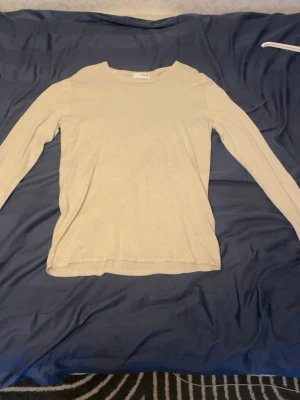 Beige långärmad tröja från SELECTED - En enkel och stilren beige långärmad tröja från SELECTED. Tröjan har rund halsringning och är gjord i ett mjukt och tunt material som passar perfekt för lager-på-lager. Snygg att matcha med jeans eller chinos. Storlek L