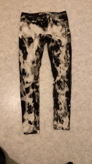 Svarta skinny jeans med bleach-mönster - Unika svarta skinny jeans med blekta vita och grå splash-effekter över hela byxan. Tight passform och klassisk femficksmodell. Perfekta för dig som vill sticka ut med en edgy och kreativ stil.