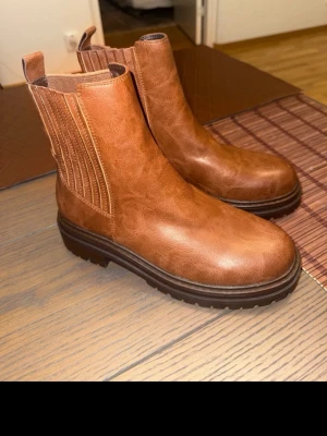 Xit  boots i läder - Snygga bruna xit boots med elastiska paneler på sidorna och robust sula. Boots i klassisk design med dragflik bak för enkel påtagning. Tillverkade i läder med en matt finish och diskreta sömmar. Perfekta för dig som vill ha stilrena och bekväma skor.