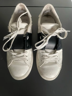 Valentino vita sneakers med svart detalj - Snygga vita sneakers från Valentino med bred svart läderdetalj. Den är använd men har inga större defekter. Storlek 38 men kan även passa som 39💕💕man får med sig den röda valentino boxen. hör av vid frågor🥰BUDA!!