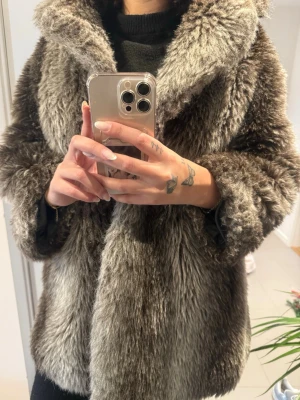 Gråbrun fluffig pälsjacka - Säljer en supermjuk och fluff sop bare gråbrun pälsjacka a la vintage vibes. Jackan har bred krage, rak passform och går ner över höfterna (perfekt oversized look). Materialet är fuskpäls som känns riktigt intervenös och varm depending på vinterdagar.