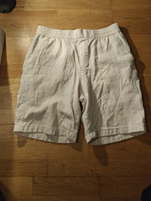 Vita linne-shorts med resårmidja - Säljer ett par ljusa, vita shorts i linne med avslappnad passform och elastisk midja. Shortsen har sidofickor och är perfekta för varma dagar. Stilrena och enkla att matcha med olika outfits.