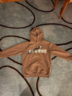 Grå demont hoodie med stjärntryck  - Säljer en grå hoodie från demont med ett stort vitt och svart stjärntryck och text på bröstet. Hoodien har en klassisk huva och en stor magficka framtill. Perfekt för dig som gillar streetwear och vill ha en skön och snygg tröja till vardags.