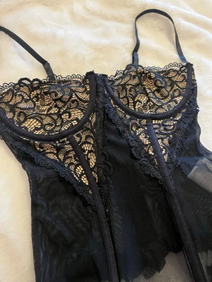 Svart korsett - Svart korsett i mesh med spets över bysten. Dragkedja bak