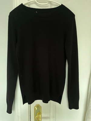 Svart basic stickad tröja - En enkel svart stickad tröja med rund halsringning och långa ärmar. Tröjan har en rak passform och små slitsar vid nederkanten. Perfekt att matcha med jeans eller kjol.