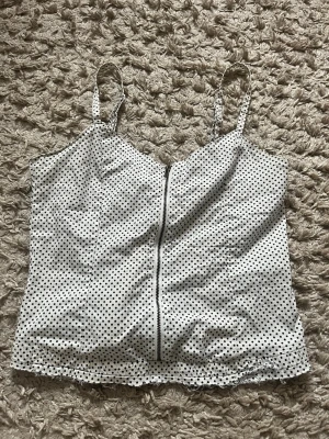 Vit prickig topp med dragkedja - Snygg vit topp med svarta prickar och smala justerbara axelband. Toppen har en dragkedja framtill och resår baktill så den passar många. Jag har storlek xs/s och den passar mig bra. Perfekt att matcha med jeans eller kjol, superfin till sommaren!🩷🩷🩷
