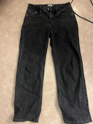 Svarta raka jeans - Säljer ett par svarta jeans med rak passform och klassisk femficksdesign. Jeansen har knappgylf och bälteshällor. Materialet är denim i bomull och färgen är tvättad svart för en avslappnad look.