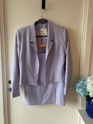 Ljuslila kavaj och kjol-set - Elegant, vintage ljuslila kostymset från Jane Simons med kavaj och matchande kjol💜  Kavajen har tre vita knappar, klassisk krage och figurnära passform. Kjolen är rak med en diskret slits framtill. Materialet är mjukt och känns som bomull, perfekt för vår och sommar.  Aldrig använd, endast testad. Passar strl 38/40!