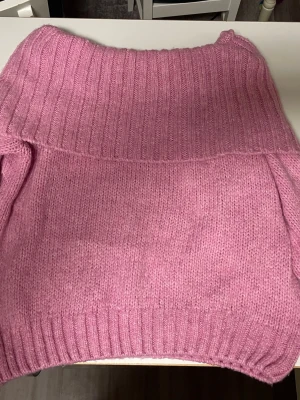 Rosa stickad polotröja - Mysig rosa stickad polotröja med bred ribbad krage och muddar. Tröjan har en avslappnad passform och är tillverkad i ett mjukt garn som känns skönt mot huden. Perfekt för kyliga dagar när du vill vara både varm och snygg.