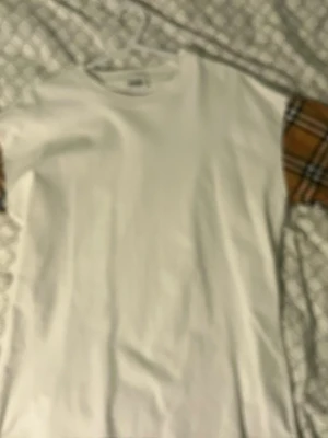 Vit t-shirt med rutiga ärmar - Vit t-shirt med klassisk passform och korta ärmar. Ärmarna har ett rutigt mönster i brunt, svart och vitt som ger en cool kontrast till den vita basen. Perfekt för dig som vill sticka ut lite extra. Materialet känns som bomull. Burbery t shirt 