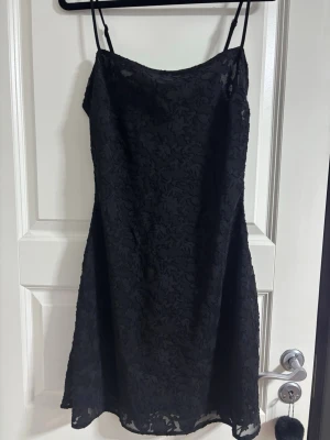 Svart spetsklänning med smala band - Snygg svart klänning från Bik Bok med smala axelband och vacker spetsdetalj över hela plagget. Klänningen har en lätt utställd form och är perfekt för dig som vill ha en stilren men ändå elegant look. Passar till många olika tillfällen.