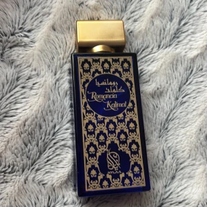 Romancia Kalimat parfym blå/guld - Lyxig parfymflaska från Nylaa i djupblått glas med detaljerat guldmönster och fyrkantig guldfärgad kork. Flaskan har orientaliska inslag och elegant design, perfekt för dig som gillar unika dofter och snygga flaskor i badrumshyllan.
