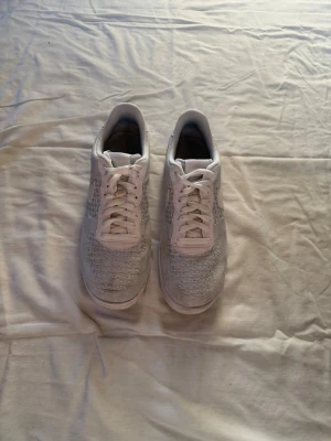 Nike Air Force 1 - Säljer ett par vita Nike Air Force 1 Flyknit sneakers med klassisk låg siluett. Skorna har stickad ovandel för extra andningsförmåga och komfort, samt vita skosnören och sula. Perfekta för dig som gillar stilrena och lätta sneakers.