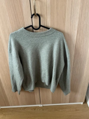 Gråmelerad stickad tröja - En enkel och stilren gråmelerad stickad tröja med rund halsringning och ribbade muddar. Tröjan har en avslappnad passform och långa ärmar, perfekt för lager på lager under kyliga dagar.