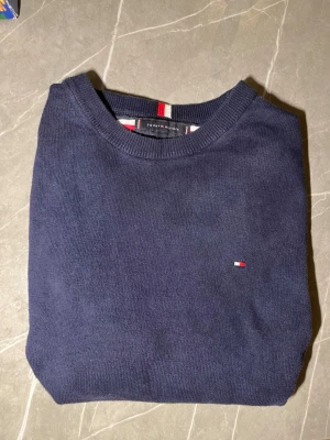 Mörkblå tröja från Tommy Hilfiger - Klassisk mörkblå tröja från Tommy Hilfiger med rund halsringning och diskret logga broderad på bröstet. PRIS KAN DISKUTERAS!!