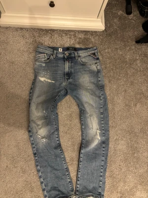 Blå slitna jeans från replay - Säljer ett par blå jeans från Replay med slitna detaljer och klassisk femficksmodell. 