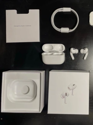 Apple AirPods Pro med laddningsetui - Säljer ett par vita Apple AirPods Pro med tillhörande laddningsetui och originalförpackning. Hörlurarna har en stilren och kompakt design med silikonpluppar för optimal passform. Materialet är blankt plast och medföljande kabel ingår.