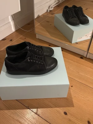 Lanvin Paris svarta - Stilrena svarta sneakers i mocka med lågt skaft. Storlek 44 passar 45 utmärkt. Nypris ca 5000kr. Köpt från NK i Stockholm. Box och allt följer med inklusive nya snören. Sparsamt använda, lite slitna i sulan därav priset men inget som syns eller märks när man gått in skorna lite.