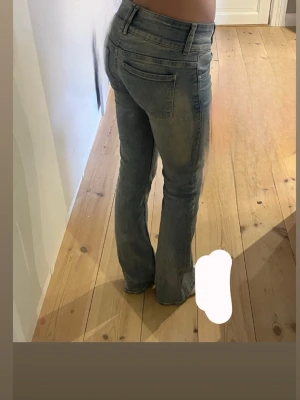 Blå bootcut jeans med dubbla knappar - Säljer ett par ljusblå bootcut jeans med dubbla knappar i midjan och klassiska fickor både fram och bak. Jeansen har en lätt tvättad look och är tillverkade i denim med lite stretch för skön passform.
