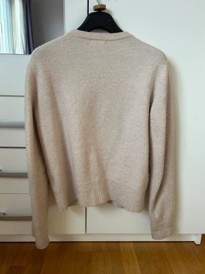 Beige kofta med knappar - Mysig beige kofta med rund halsringning och knäppning framtill. Koftan har långa ärmar och ribbade muddar vid ärmslut och nederkant. Perfekt för lager på lager och enkel att matcha med olika outfits.