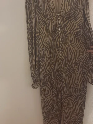 Adoore klänning  - Snygg långklänning med zebramönster i beige och brunt. Klänningen har v-ringning, långa ärmar och knappar framtill. Perfekt för dig som vill sticka ut med ett djurmönster och en avslappnad men trendig look. Klänningen är köpt för 1690 kr och Eftersom klänningen är i fint skick och vill köpa ny i rätt storlek säljs klänningen för 1100 kr , hör av er vid funderingar 🌸 storlek 40