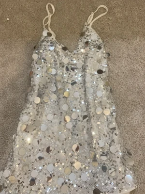 Glittrig paljettopp med smala band - Säljer en superglittrig topp med smala axelband, täckt av stora och små silverpaljetter på vit botten. Toppen har v-ringning och är perfekt för dig som vill sticka ut. Materialet känns lätt och skimrande. vet inte vilket märke den är ifrån då jag köpte den någonstans på nätet för en konsert men den är i supermjukt material och passar superfint!