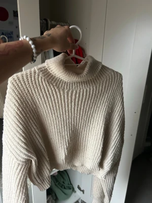 Krämvit croppad polotröja stickad - Säljer en krämvit croppad stickad polotröja med breda ärmar och ribbad struktur. Tröjan har en hög krage och är perfekt för lager på lager. Materialet känns mjukt och mysigt, och modellen är oversized för en avslappnad look. Använd väl men i bra skick, säljer då den inte används mer. Priset som syns är vad som gäller och frakten står köparen för🤍🤍🤍🤍🤍
