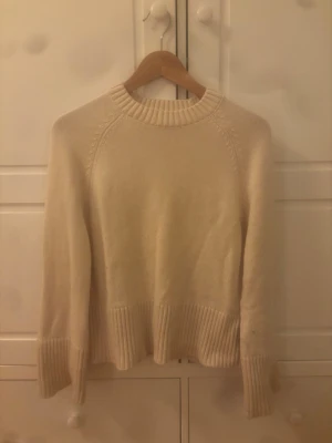 Beige oversized stickad tröja - Mysig beige stickad tröja med bred ribbad kant vid ärmslut och nederkant. Tröjan har en avslappnad, oversized passform och rund halsringning. Perfekt för lager på lager och enkel att matcha med jeans eller kjol.