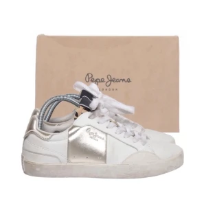 Pepe jeans sneakers - Stilrena vita sneakers från Pepe Jeans med metallic-detaljer i guld på sidan och hälen. Klassisk låg modell med vita skosnören och diskret logga på sidan. Ovandelen är i läder och syntet, med leopardmönstrad detalj på plösen för extra edge.