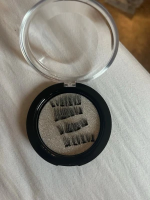 Magnetiska lösögonfransar i ask - Säljer ett set med magnetiska lösögonfransar i svart. Fransarna kommer i en rund, svart ask med genomskinligt lock och ligger på en glittrig silverbotten. Perfekt för dig som vill ha fylligare fransar utan lim. Lätta att applicera och ta bort.