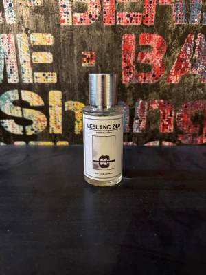 LEBLANC 24.0 Eau de Parfum - LEBLANC 24.0 Eau de Parfum i en stilren, genomskinlig glasflaska med silverfärgad metallkork. Flaskan har en minimalistisk etikett med svart text och en grafisk illustration. Perfekt för dig som gillar unika och moderna dofter.