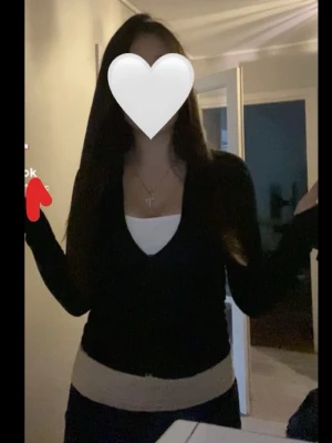 Svart kofta - Stilren svart kofta med långa ärmar. Koftan har en figurnära passform och bärs här över ett vitt linne. Perfekt för lager på lager och enkel att matcha med olika outfits.