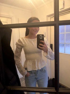 Vit smockad blus med volang - Säljer en vit blus med smockad överdel och volang nertill. Blusen har rund halsringning och långa ärmar med lätt puff och rynkade detaljer. Materialet ser ut att vara bomull eller liknande och ger en romantisk känsla.