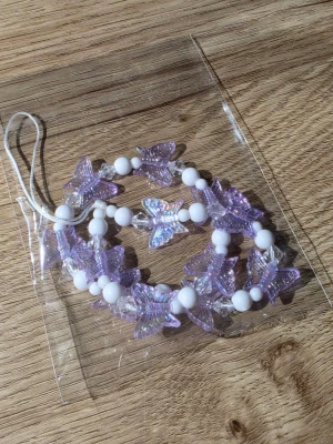 Lila fjärilsdekor till mobil - Söt mobildekor med lila genomskinliga fjärilar och vita pärlor på elastisk tråd. Perfekt att hänga i mobilen för en personlig touch. Passar de flesta mobilmodeller och ger en trendig look.