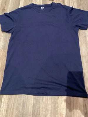 Mörkblå basic t-shirt från 157 - En enkel och stilren mörkblå t-shirt från 157. T-shirten har rund halsringning och korta ärmar. Tillverkad i mjuk bomull som känns skön mot huden. Perfekt till jeans eller shorts för en clean look.