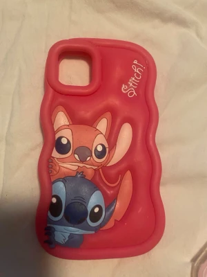 Rosa Stitch mobilskal med motiv - Säljer ett rosa mobilskal med motiv av Stitch och Angel från Disney. Skalets form är vågig och det är gjort i mjukt silikonmaterial som ger bra grepp. Perfekt för dig som gillar söta och färgglada accessoarer till mobilen. Passar till IPhone 11