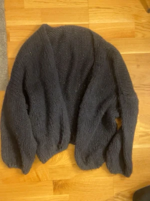 Marinblå stickad kofta - Mysig marinblå stickad kofta med lös passform och långa ärmar. Koftan är öppen framtill och har en enkel, klassisk design som passar perfekt till lager på lager. Materialet känns mjukt och värmande, perfekt för kyliga dagar. STORLEK XS-M