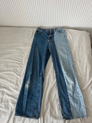 Tvåfärgade raka jeans - Unika tvåfärgade jeans med ena benet i mörkblå denim och det andra i ljusblå denim. Raka ben och klassisk femficksmodell. Perfekta för dig som vill sticka ut med en cool och trendig look. Jeansen är lite slitna både bak och fram vilket man kan se på bilderna men i övrigt väldigt fina jeans.