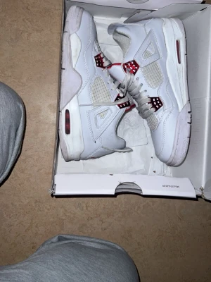 Jordan 4 , red and white. - Säljer ett par vita Air Jordan 4 Retro sneakers med röda och grå detaljer. Skorna har meshpaneler på sidorna, synlig Air-enhet i sulan och klassiska plastdetaljer vid snörningen. Perfekta för dig som gillar streetwear och ikonisk design.